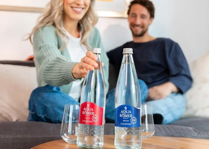 Ein Paar genießt Aqua Römer Mineralwasser auf dem Sofa.